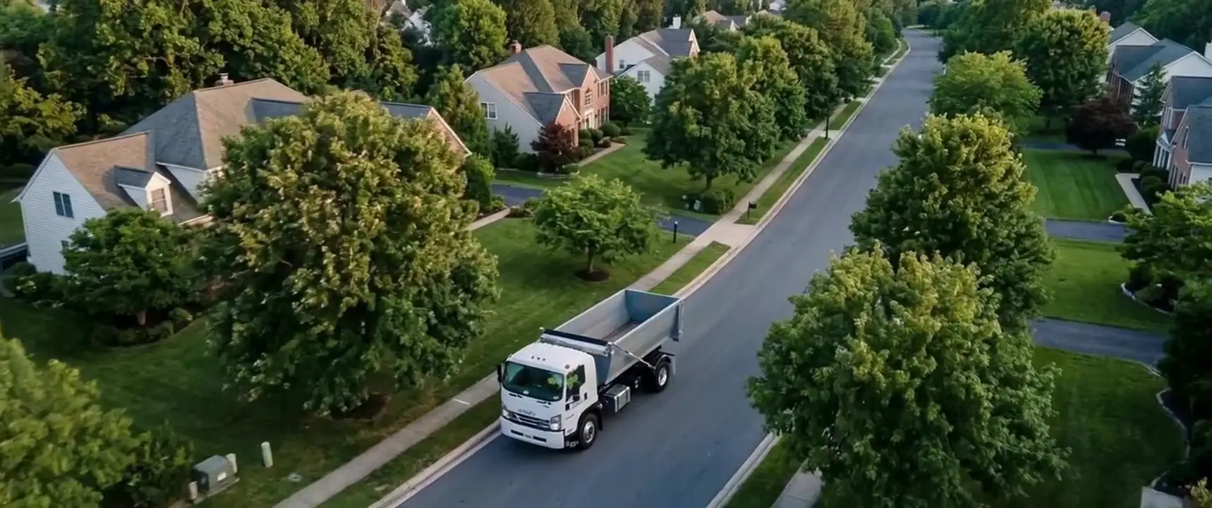 Roll off truck driving through a tree-lined suburban neighborhood
