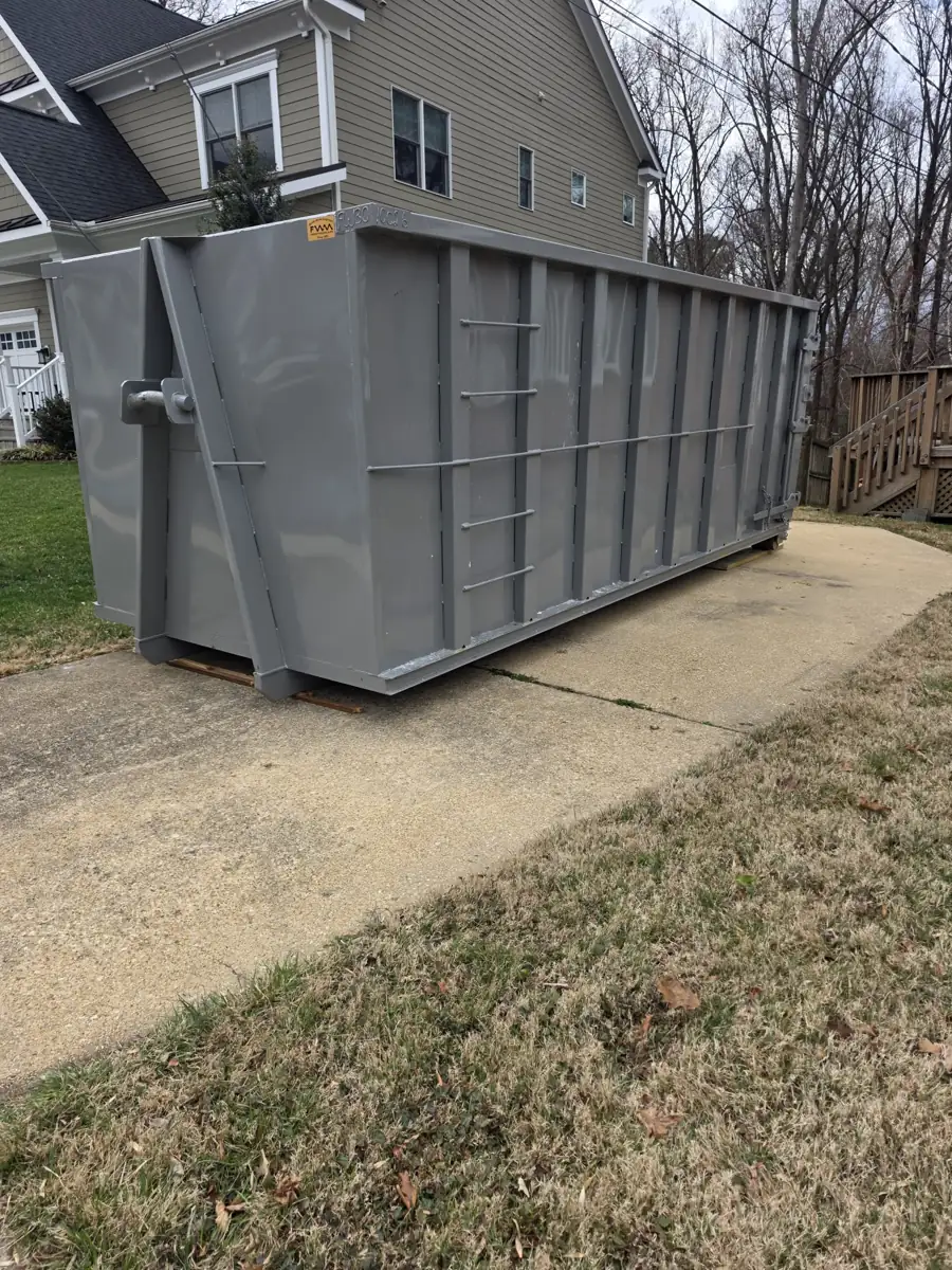 Gray roll off container on a concrete driveway beside a house in Gaithersburg, MD