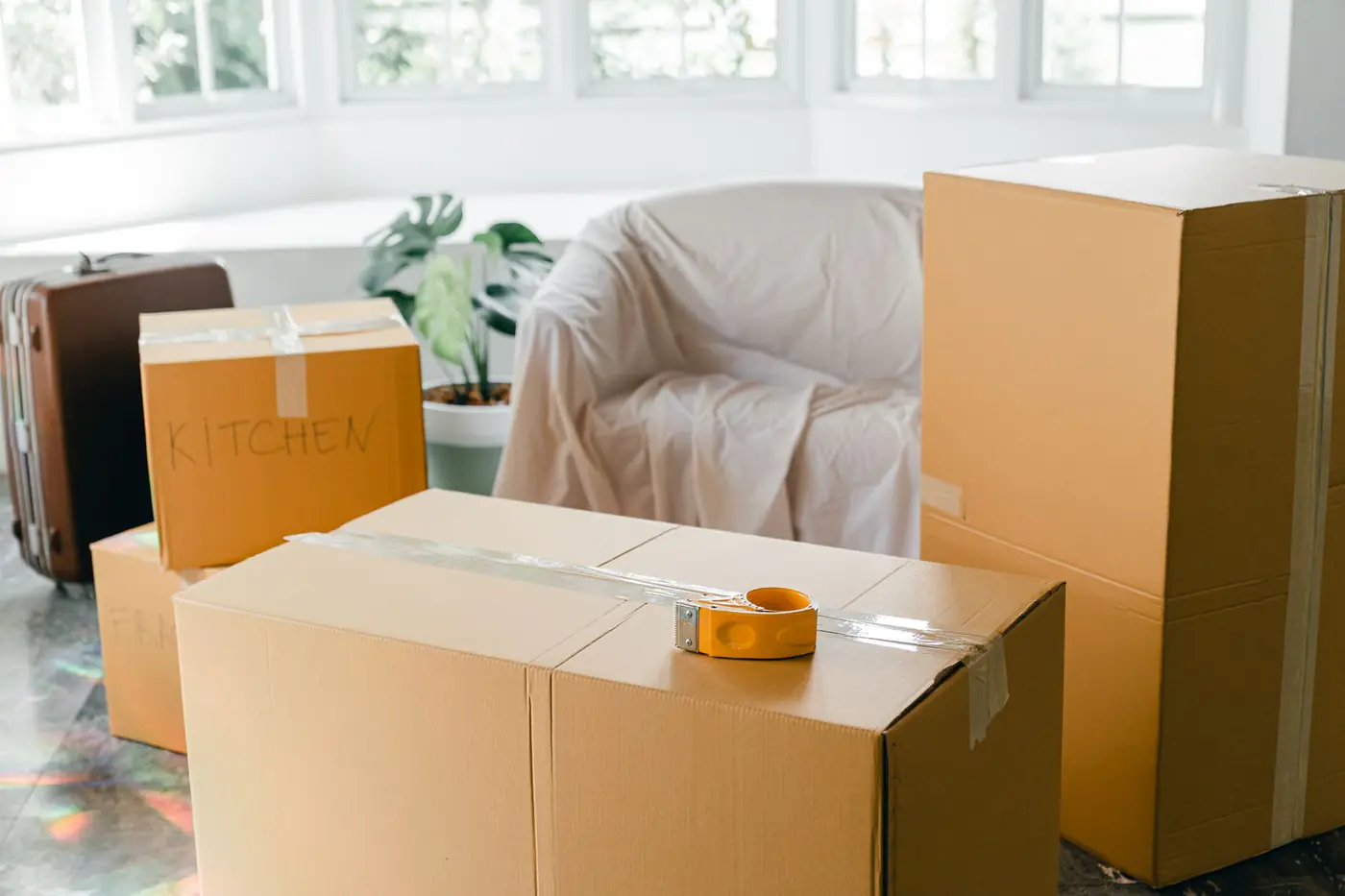 Taped moving boxes, a suitcase and a covered armchair in a bright room during a move