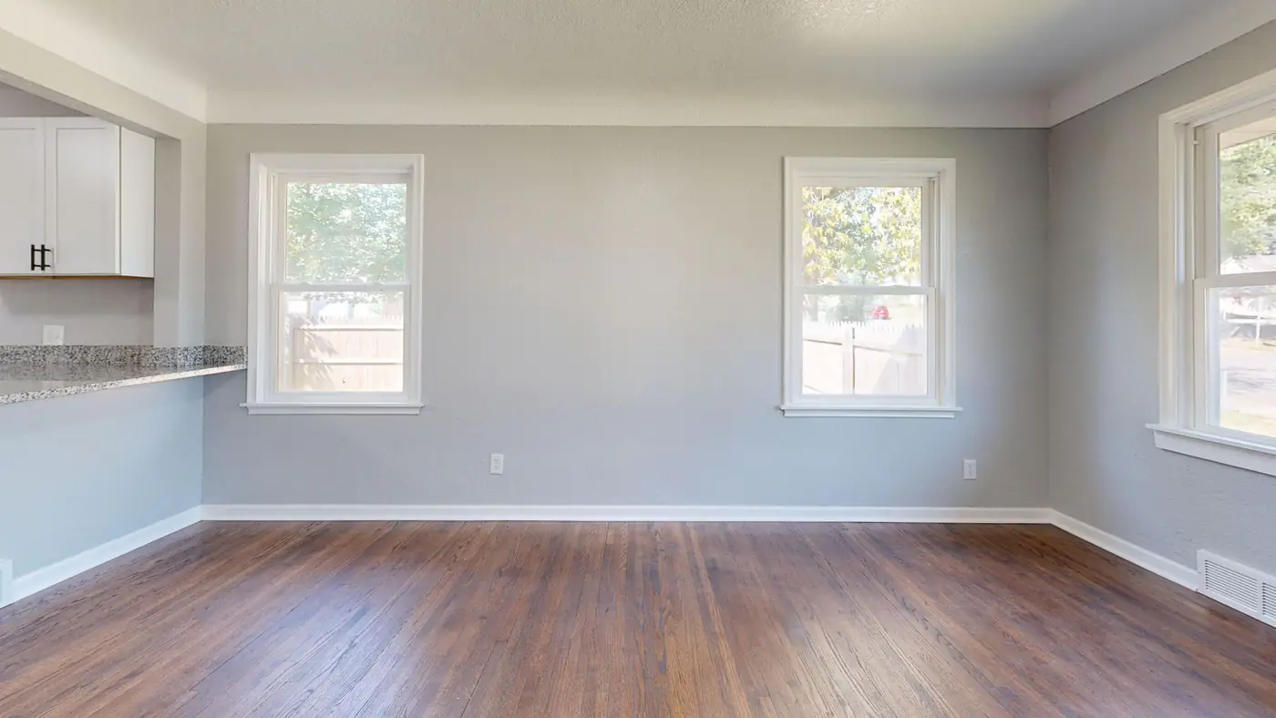 Empty apartment living room with gray walls, wood floors and a kitchen counter, ready for new tenants