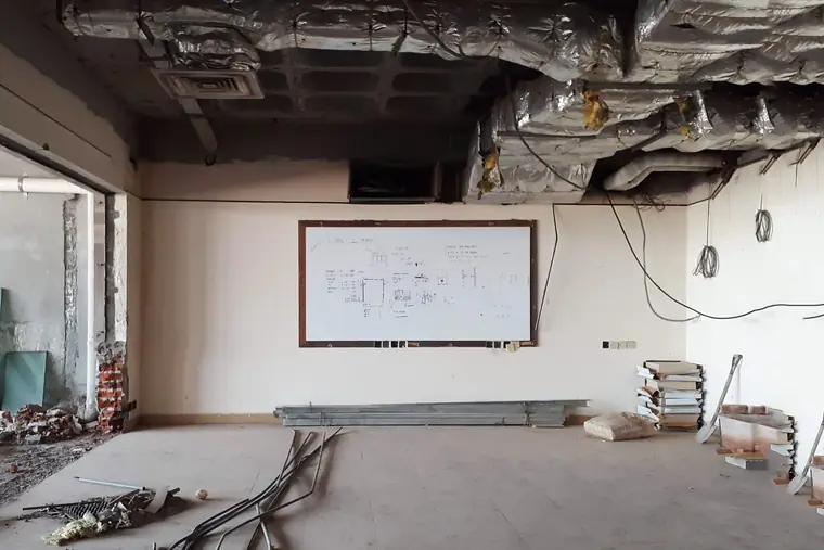 Commercial space mid renovation with ceiling panels removed, exposed ductwork and materials stacked on the floor