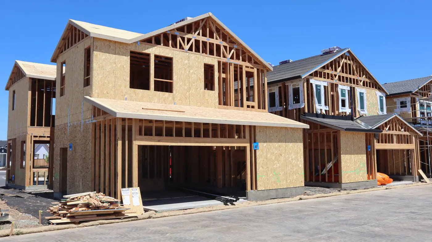 Row of two-story homes being framed with sheathing, open garages and scrap lumber by the street