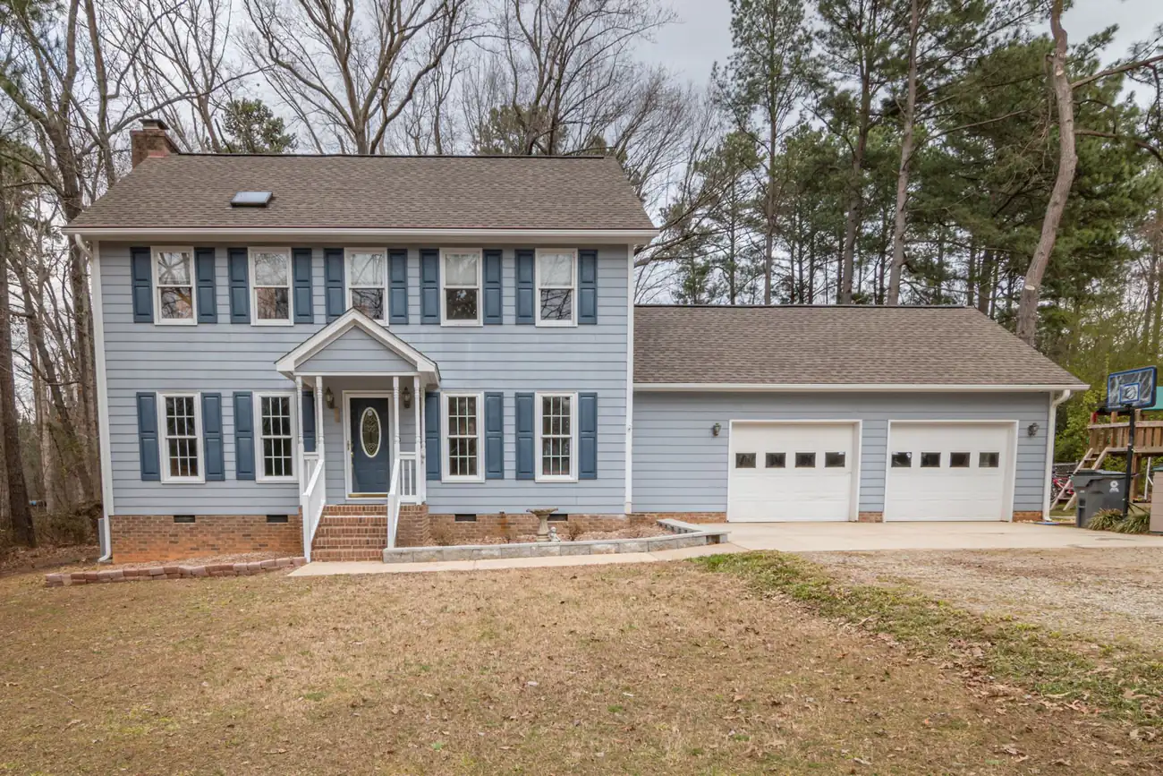 Blue two-story colonial with shutters, an attached two-car garage and a wide concrete driveway