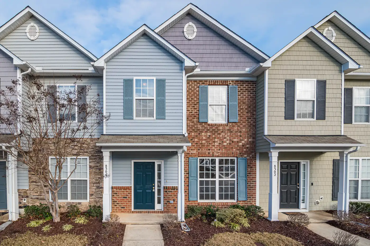 Row of townhouses with brick, blue and tan siding, shutters and small front gardens