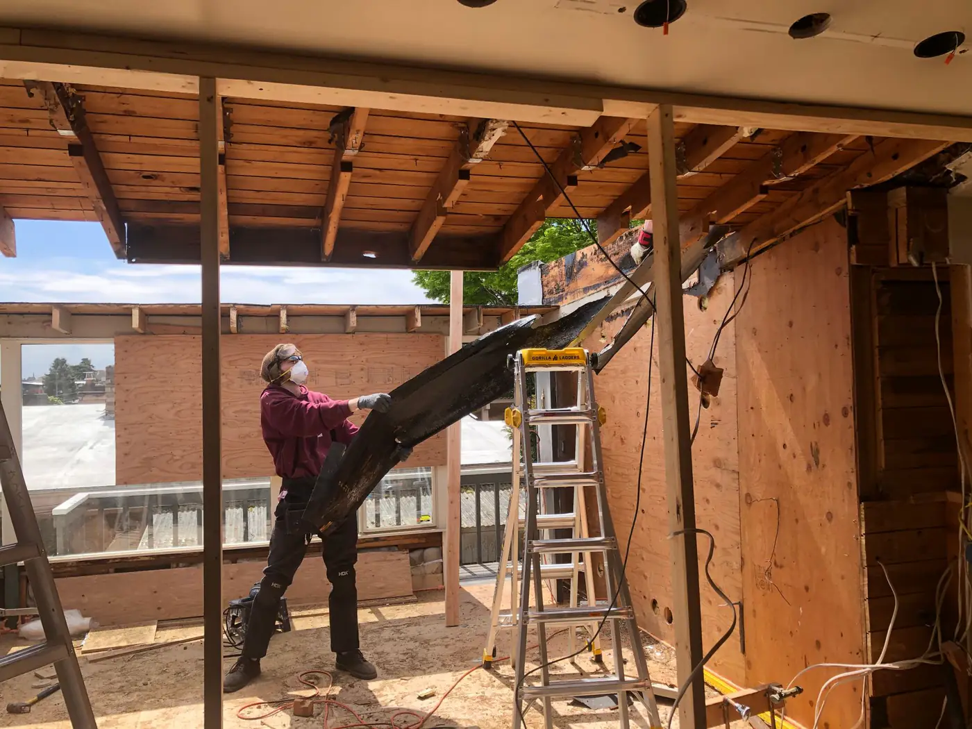 Worker in a dust mask pulling down old ceiling boards during a home renovation, with a ladder nearby